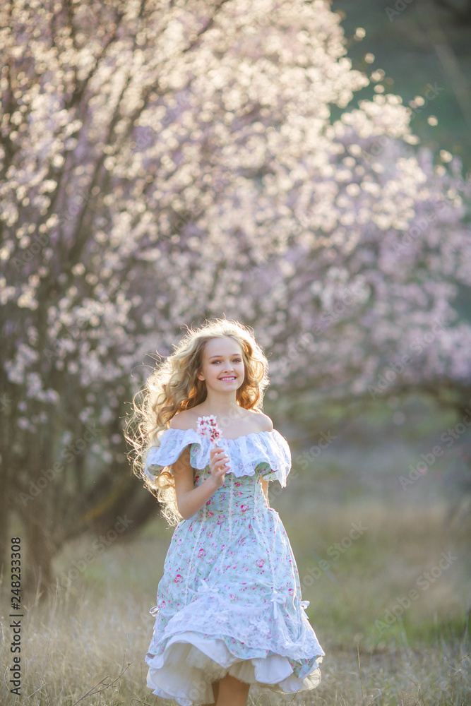 Sweet woman in a beautiful dress, walking through the park with flowers in hands