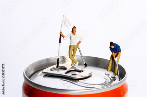 Conceptual diorama image of a miniture figure couple playing golf on a drinks can