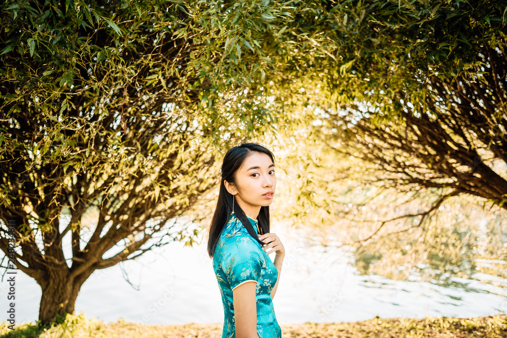 Portrait of beautiful Asian Chinese brunette in blue national dress outdoors, young Vietnamese woman in traditional clothes, the girl is resting in park Portrait of beautiful Asian Chinese brunette in blue national dress outdoors, young Vietnamese woman in traditional clothes, the girl is resting in park