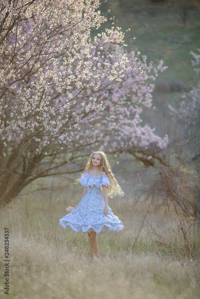 A young long-haired blonde is walking in a blooming garden. Dress and hair fluttering like in a fairy tale A young long-haired blonde is walking in a blooming garden. Dress and hair fluttering like in a fairy tale