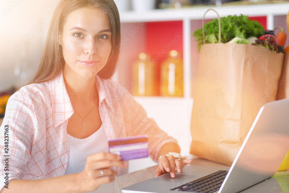 Smiling woman online shopping using tablet and credit card in kitchen . Smiling woman Smiling woman online shopping using tablet and credit card in kitchen . Smiling woman