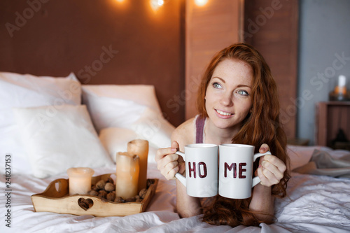 Morning in bed, a young charming red-haired woman with freckles lying in bed, hugging pillow, smiling, enjoying the morning