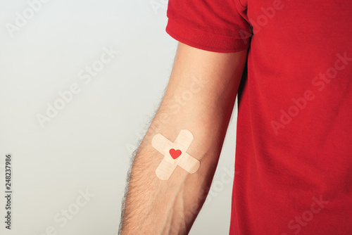 Fototapet Partial view of patient in red t-shirt with plasters on grey background, blood d