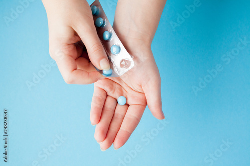 Hands opening a package of blue pills against a blue background