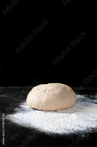 Dough with spilled flour on a black background. Yeast dough for bread, rolls, pizza, focaccia or pie. Homemade dough. Copy space.