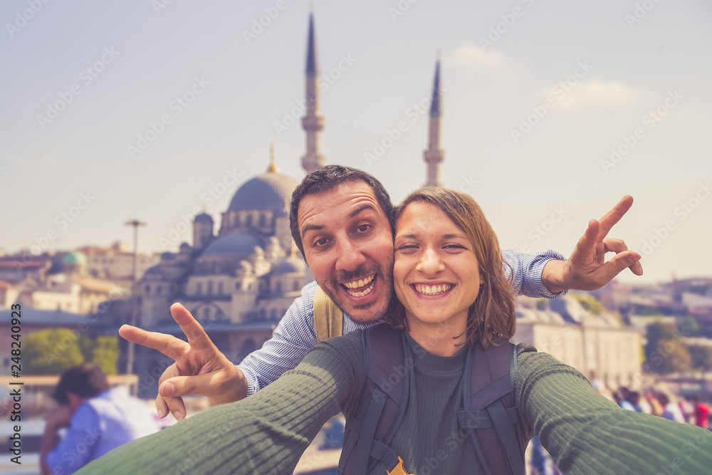 Fototapeta premium Happy young couple taking a selfie photo in Istanbul, Turkey. Two smiling tourists with smart phone taking selfie in front of the Blue Mosque in Istanbul. Travel and vacation around concept 