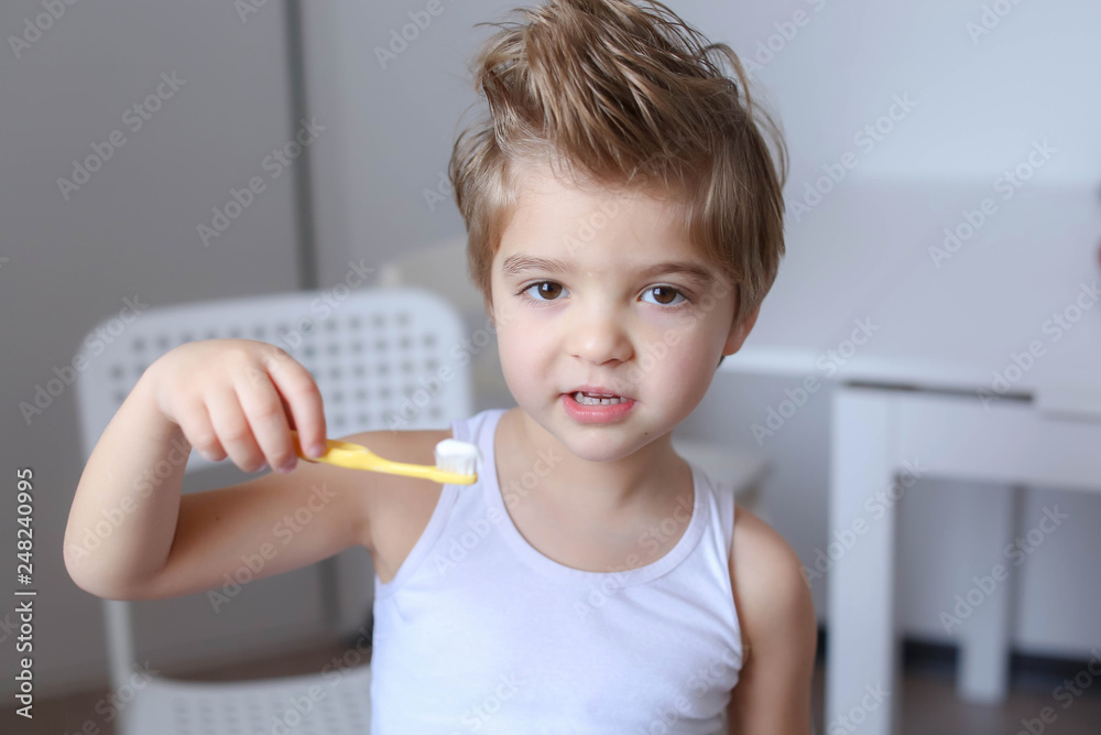 Close up portrait of cute, adorable, toddler boy wearing denim overalls, long T-shirt, sitting on the floor, brushing his teeth with a toothbrush Close up portrait of cute, adorable, toddler boy wearing denim overalls, long T-shirt, sitting on the floor, brushing his teeth with a toothbrush
