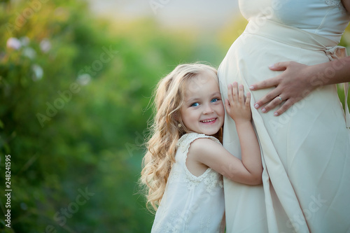 Happy family: a young beautiful pregnant woman with her little cute daughter walking in the wheat orange field on a sunny summer day. Parents and kids relationship. Nature in the country.