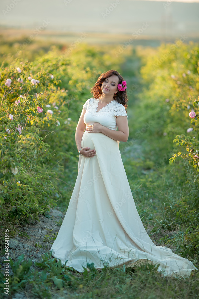 Outdoor natural portrait of beautiful pregnant woman in white dress
