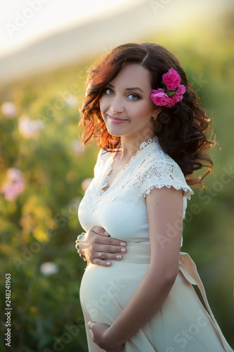 Outdoor natural portrait of beautiful pregnant woman in white dress