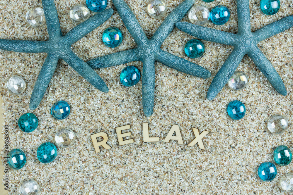 relax wooden letters on a background of sand, teal blue starfish and glass baubles relax wooden letters on a background of sand, teal blue starfish and glass baubles