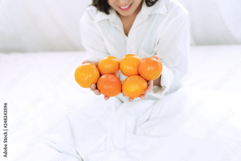 Lifestyle and healthy food concept. Focus hands of smile young woman holding fresh oranges fruit in her hand on white bed at home with copy space. Lifestyle and healthy food concept. Focus hands of smile young woman holding fresh oranges fruit in her hand on white bed at home with copy space.