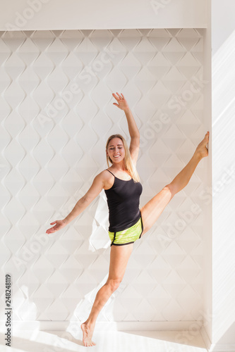 Fototapeta Naklejka Na Ścianę i Meble -  Young happy fitness model woman athlete  doing stretching workout near sunny solar bright wall. Healthy life bodybuilding lifestyle concept image, copy space. White empty background for text.