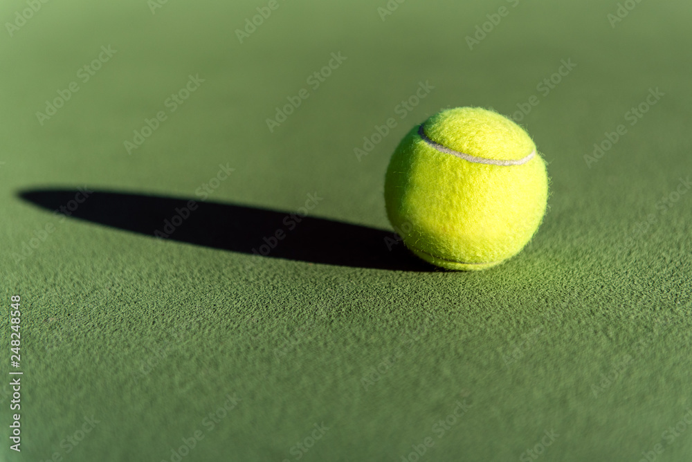 Fuzzy yellow tennis ball lying on the textured surface of court over a long  shadow. Stock Photo | Adobe Stock