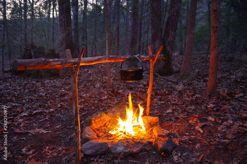 Bushcraft campfire for cooking with primitive debris hut shelter in the  background. Wilderness survival skill Stock Photo