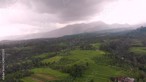 Aerial shot high above rice paddies in Bali, Indonesia, slowly tracking backwards away from the mountains and tress in South East Asia. rice farms se stacks to help the water irrigation photo