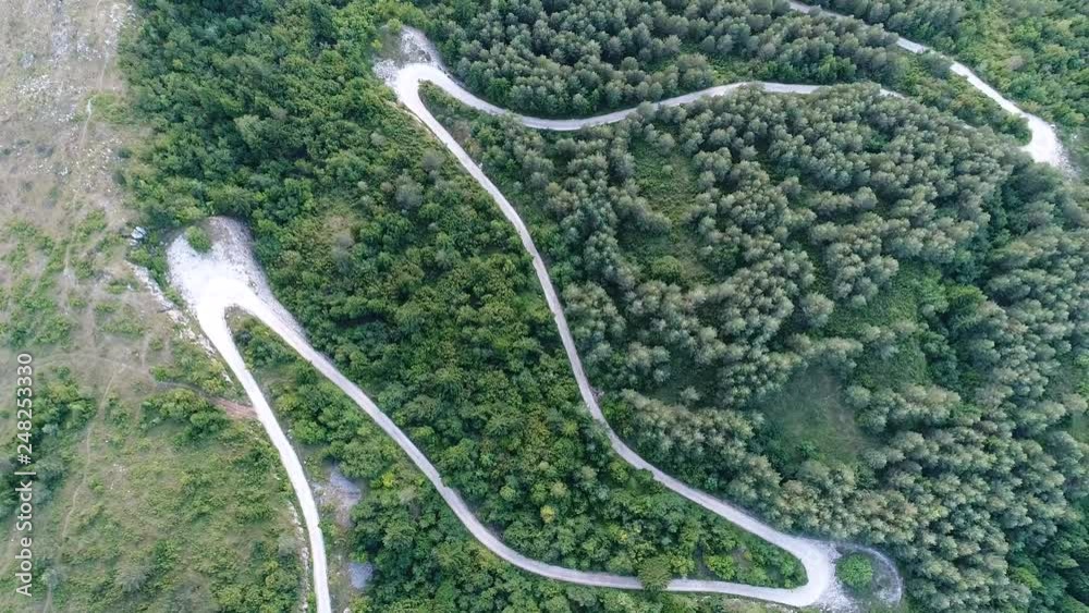 aerial view of countryside curvy road passing through the green forest and mountain on sunny summer day aerial view of countryside curvy road passing through the green forest and mountain on sunny summer day