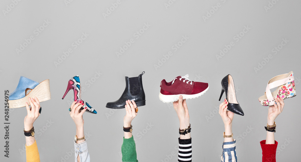 Hands holding different shoes on gray background - obrazy, fototapety, plakaty 