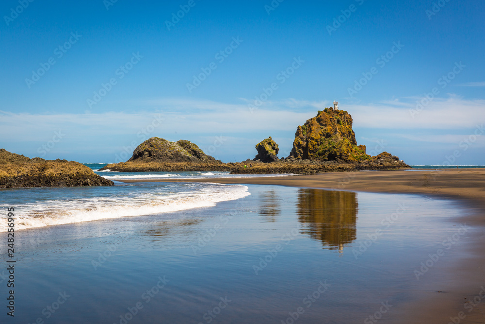 Obraz premium Whatipu Beach, New Zealand. Black sand, rock formations and white waves. Reflection on the water