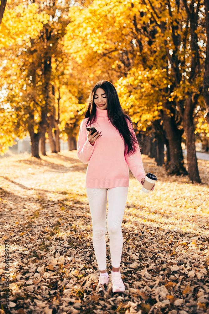 Beautiful woman drink coffee, using phone and walking in the park. Beautiful woman drink coffee, using phone and walking in the park.