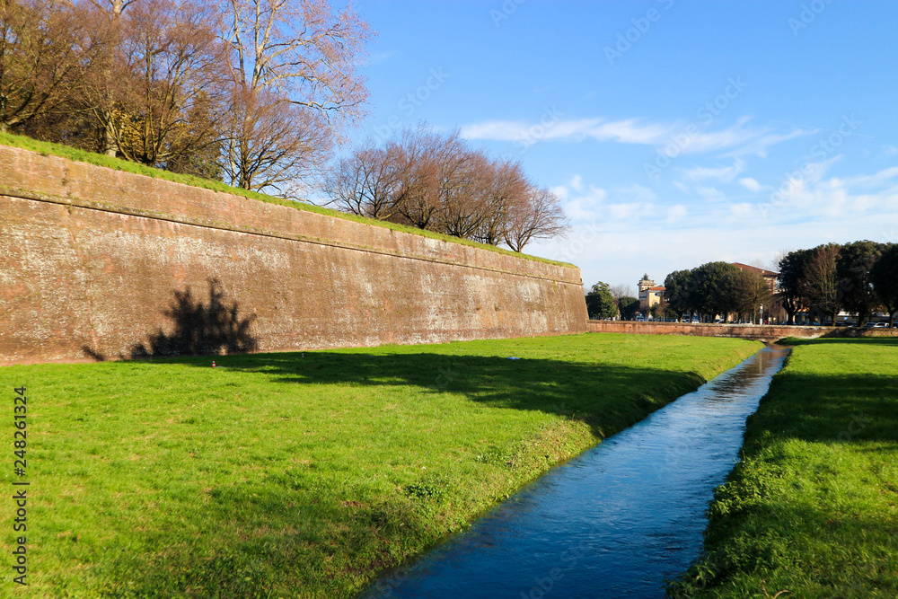 Lucca medieval city wall with green grass and old moat full of water, Tuscany, Italy