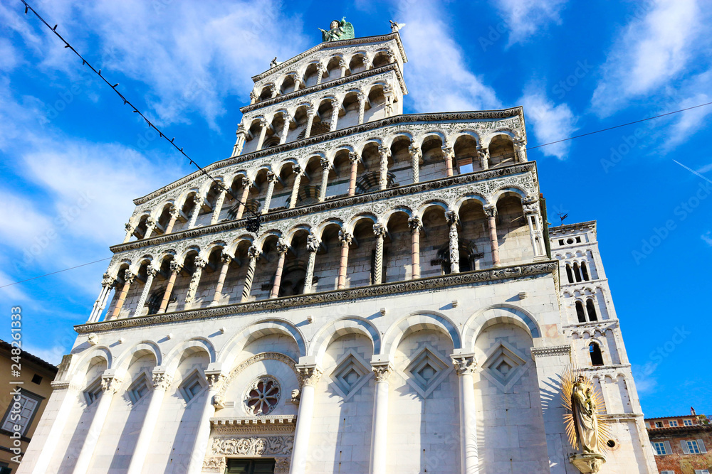 Facade with columns made from white marble of Roman Catholic basilica church San Michele in Foro in Lucca, Tuscany, central Italy with blue winter sky and clouds on the background