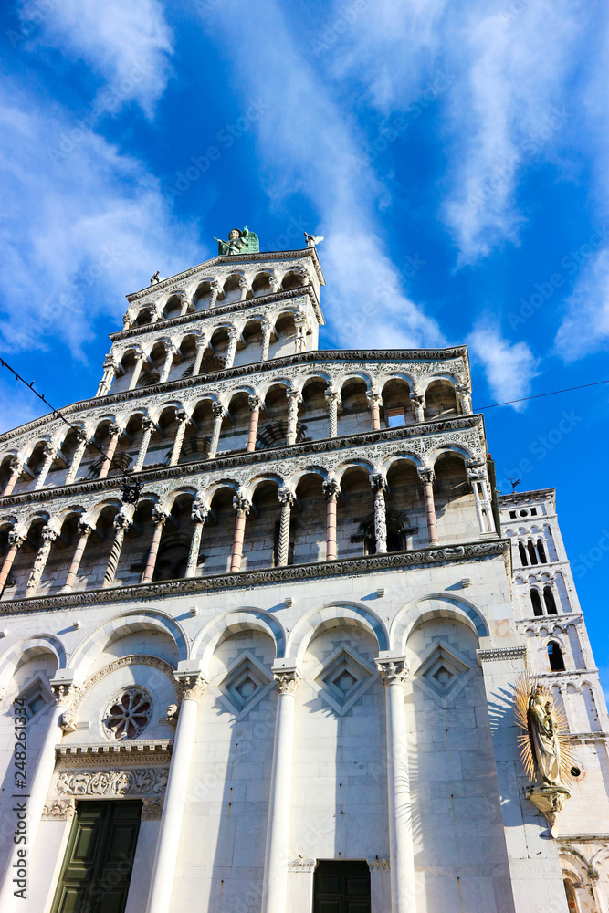 Facade with columns made from white marble of Roman Catholic basilica church San Michele in Foro in Lucca, Tuscany, central Italy with blue winter sky and clouds on the background