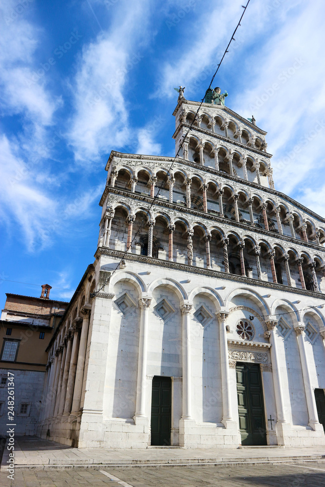 Facade of Roman Catholic basilica church San Michele in Foro in Lucca, Tuscany, central Italy with blue winter sky and clouds on the background