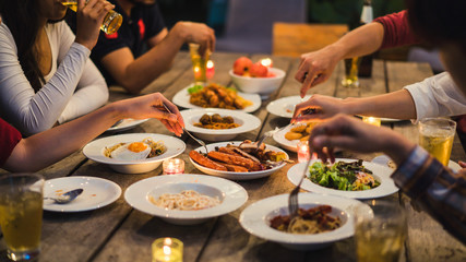 Asian group eating and drinking cold beer outside the house at night, having fun talking