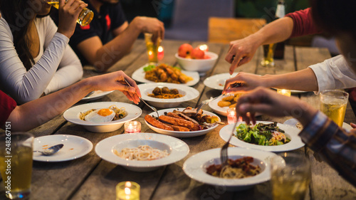 Asian group eating and drinking cold beer outside the house at night, having fun talking