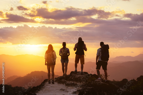 Group of four peope's silhouettes stands on mountain top and looks at sunset