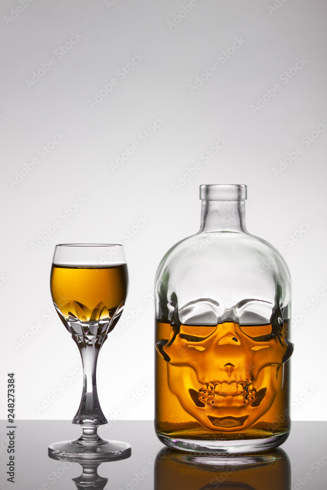 A skull bottle and crystal glasses with a liquid, alcohol drink.