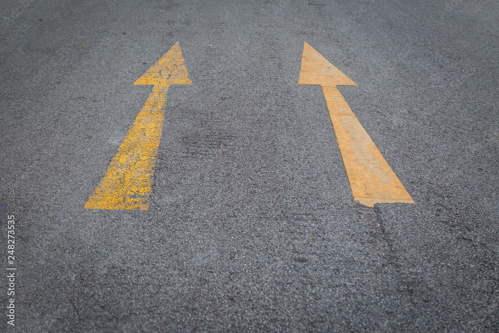 Two yellow arrows old and new  directionon asphalt road