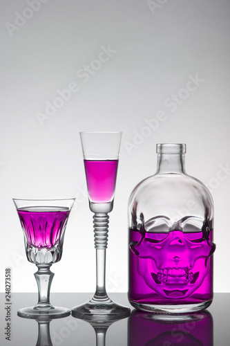 A skull bottle and crystal glasses with a liquid, alcohol drink.