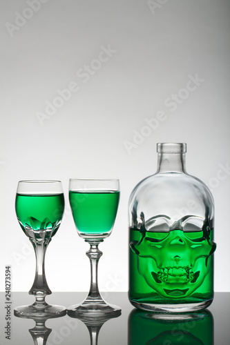 A skull bottle and crystal glasses with a liquid, alcohol drink.