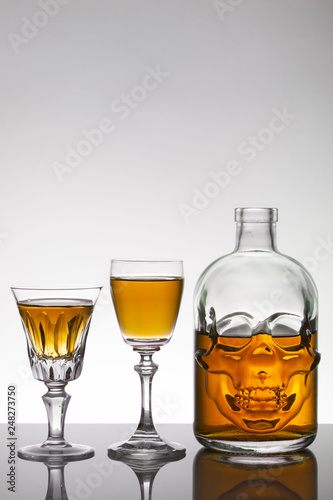 A skull bottle and crystal glasses with a liquid  alcohol drink.