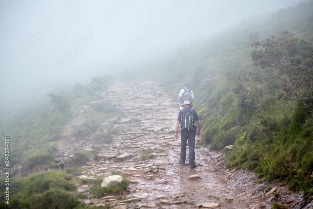 Couple of hikers walking in mountains. Hiking trail in the Pyrenees. La Rhune mountain, France Couple of hikers walking in mountains. Hiking trail in the Pyrenees. La Rhune mountain, France