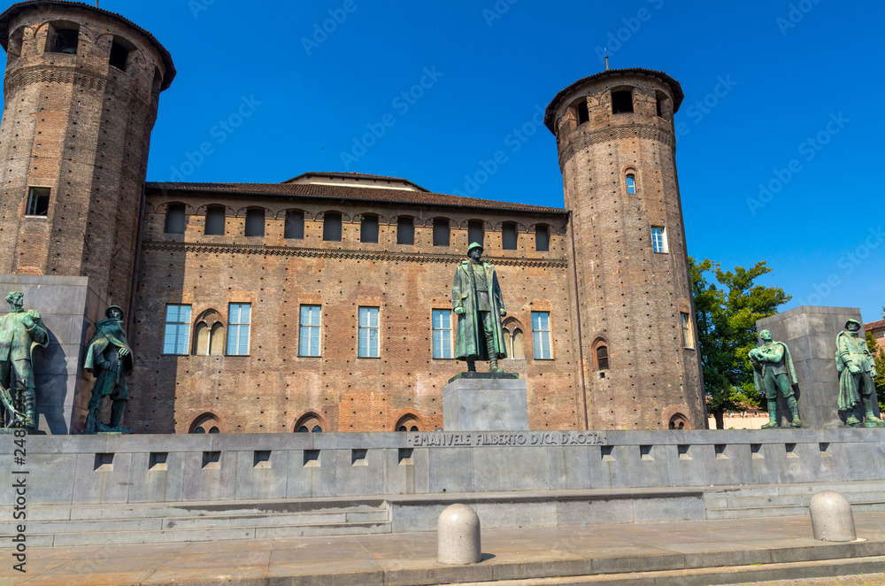 Medieval old Acaja Castle with brick towers and Monumento Emanuele Filiberto Duca d'Aosta on Castle Square Piazza Castello in historical centre of Turin Torino city, clear blue sky, Piedmont, Italy