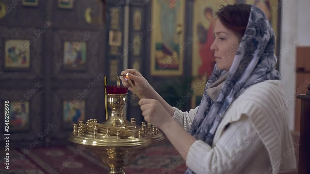 woman in the Russian Orthodox Church with red hair and a scarf on her head lights a candle and prays in front of the icon. woman in the Russian Orthodox Church with red hair and a scarf on her head lights a candle and prays in front of the icon.
