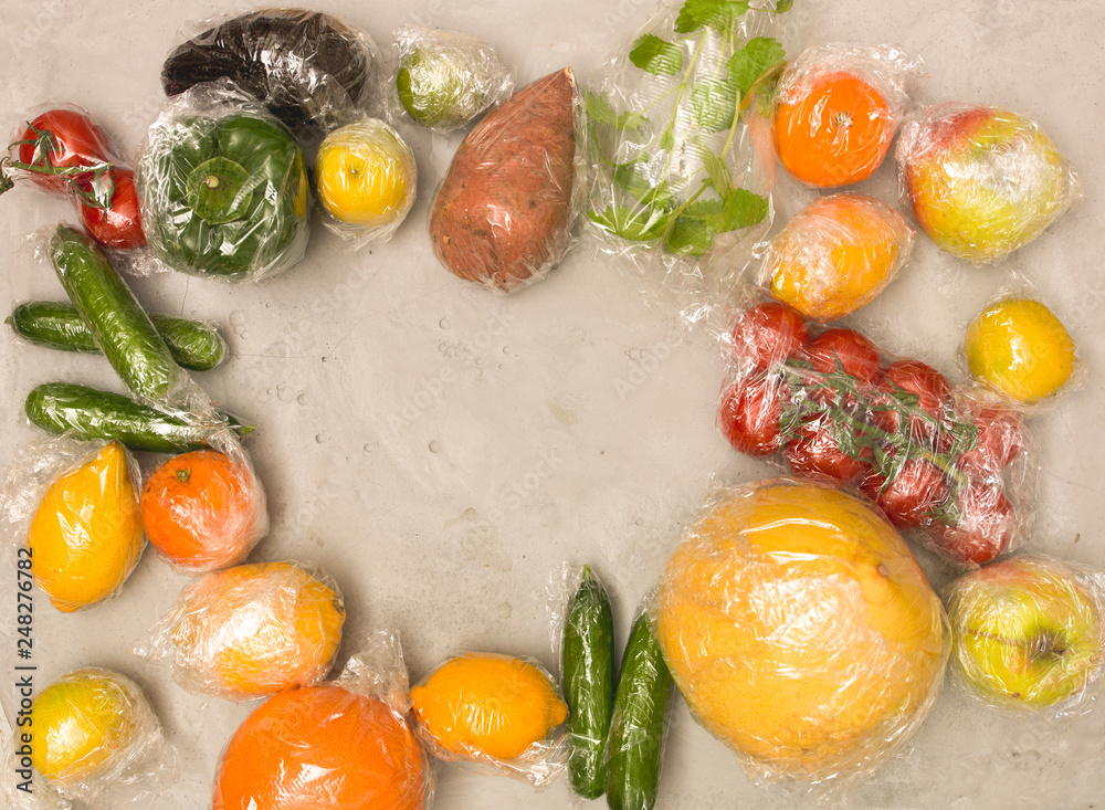 many different fruits and vegetables are wrapped in plastic foil, packed on concrete background