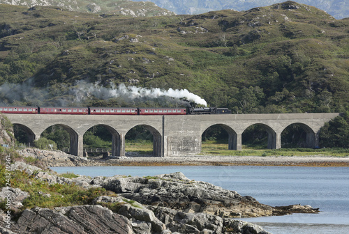 A landscape view of the Jacobite steam train crossing Loch nan umbh viaduct, Scotland, UK. photo