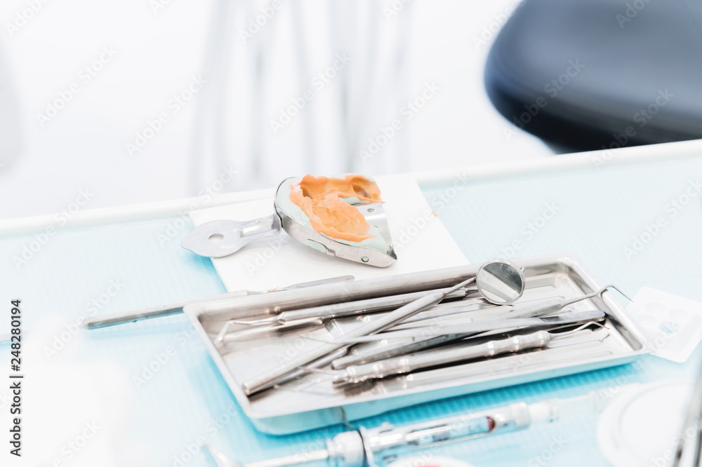 Close-up of a common stamotological instrument next to a metal form for prosthetics. Dental equipment. Dental hygiene and healthcare concept Close-up of a common stamotological instrument next to a metal form for prosthetics. Dental equipment. Dental hygiene and healthcare concept