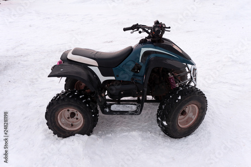Close-up ATV 4wd quad bike in forest at winter 4wd all-terreain vehicle stand in heavy snow with deep wheel track. Seasonal extreme sport adventure and trip. Copyspace