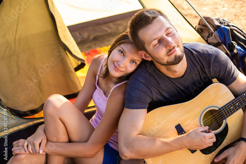 A man plays for a woman on a guitar near a tent at sunset. Honeymoon in the hike © artem_goncharov