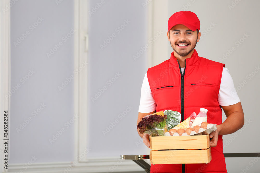 Food delivery courier holding wooden crate with products indoors. Space for text Food delivery courier holding wooden crate with products indoors. Space for text