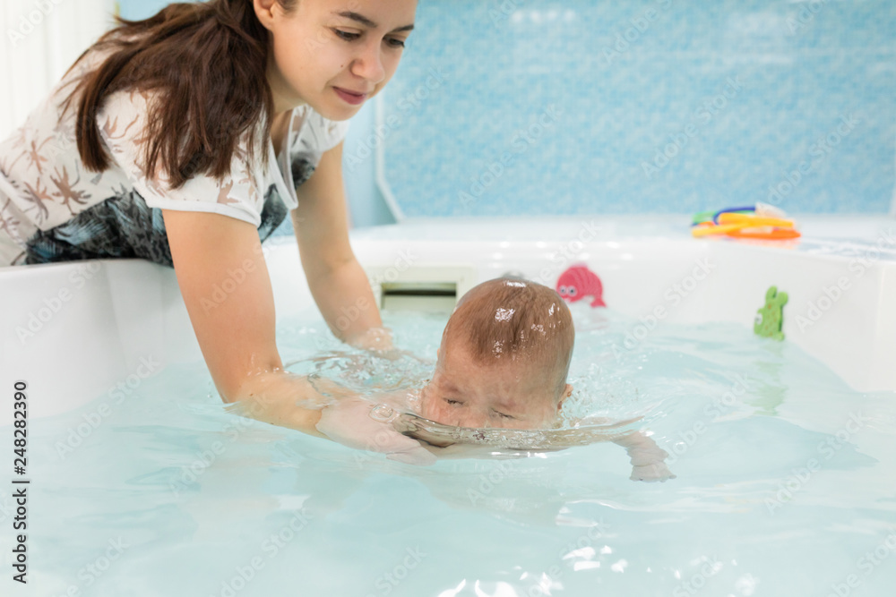 Baby boy diving under the water with mother at bath. Swimming and hardening concept Baby boy diving under the water with mother at bath. Swimming and hardening concept