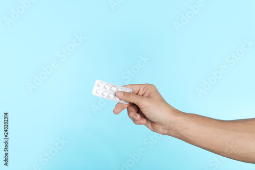 Young man holding pills on color background, closeup with space for text. Medical object