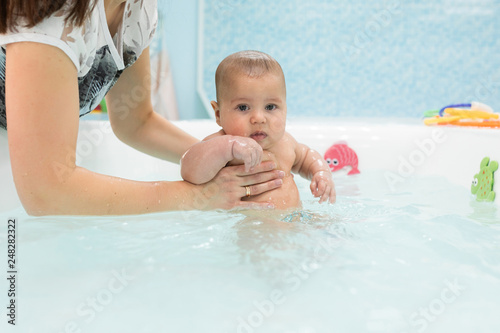 Cute baby swimming in bathroom. The instructor teaches mom infants fitness and swimming