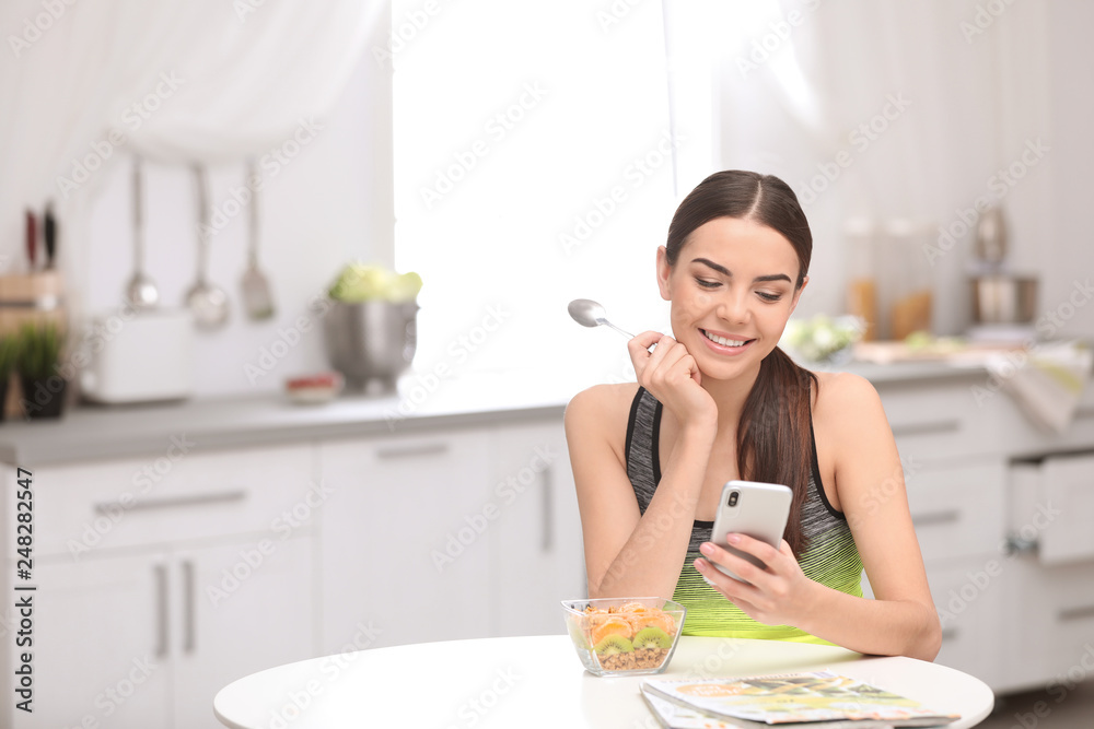 Young woman in fitness clothes using smartphone while having healthy breakfast at home. Space for text Young woman in fitness clothes using smartphone while having healthy breakfast at home. Space for text