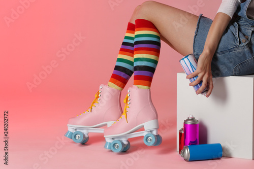 Woman with vintage roller skates and spray paint cans on color background, closeup. Space for text